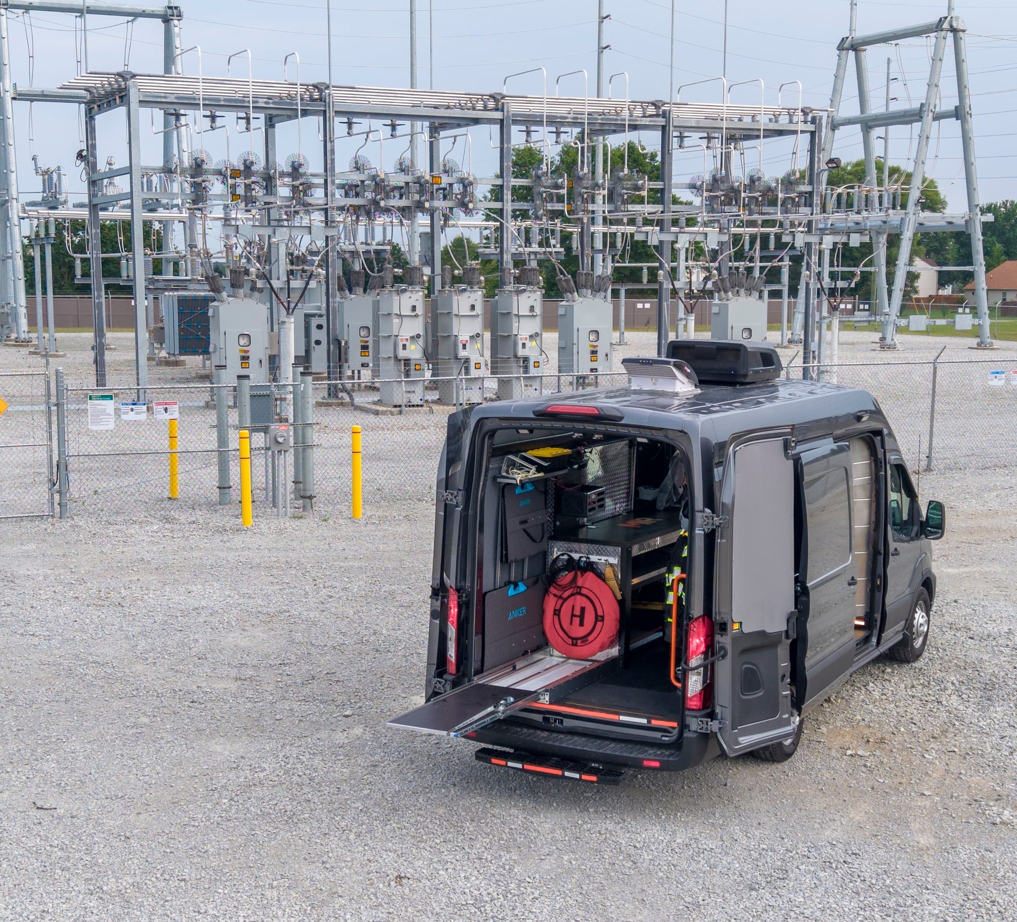 MIR command van with rear doors open and equipment staged, parked at an electrical substation switchyard with transmission structures and disconnect switches behind