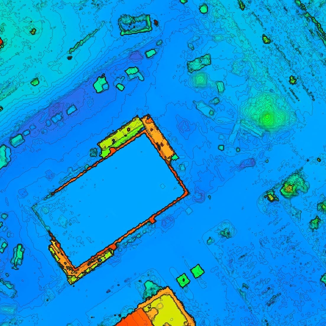 Colorized elevation model of the commercial construction site — buildings, parking, and roadways — overlaid with fine survey-interval contour lines, shaded from blue low ground through green to orange and red high ground