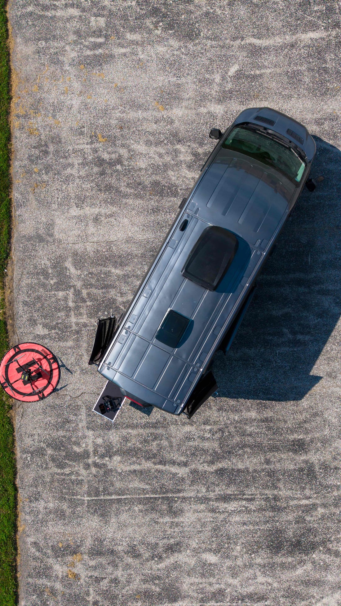 Top-down aerial of the MIR command van parked on pavement with the aircraft staged on its red landing pad
