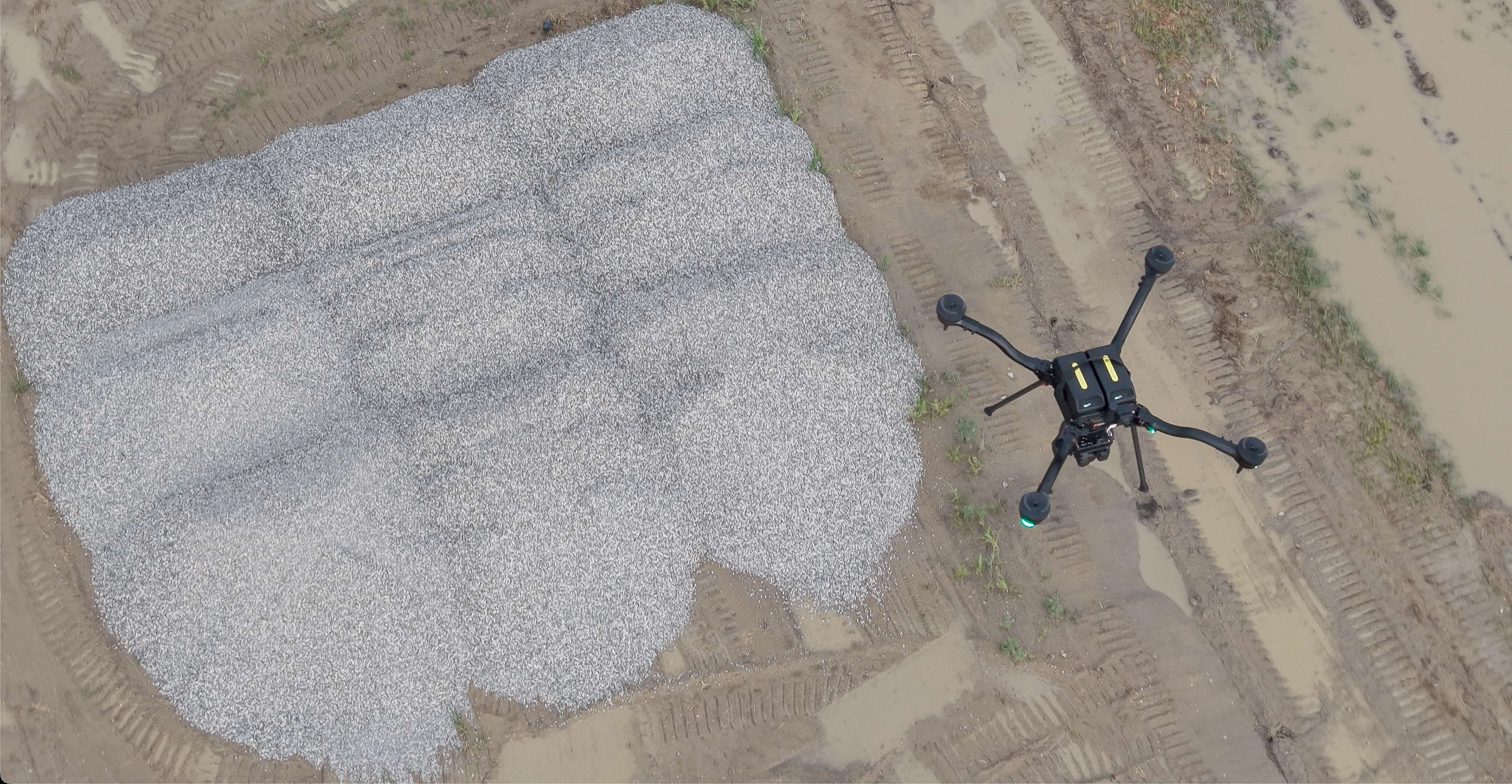 Top-down aerial of a Freefly Astro drone flying over a crushed-stone stockpile on a rutted haul yard during an RTK photogrammetry mission