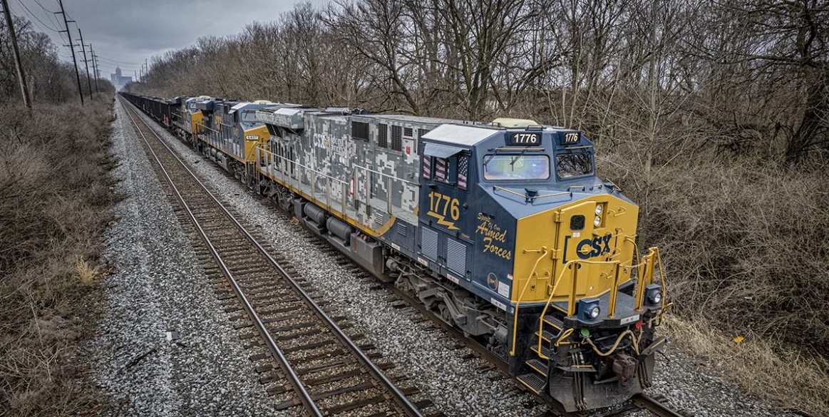 CSX freight locomotive number 1776 in Spirit of Our Armed Forces livery leading a train down the tracks through a wooded corridor