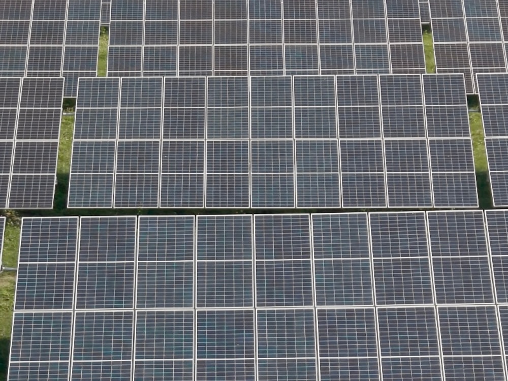 Visible-light aerial photo of a ground-mounted solar array with long rows of photovoltaic panels over grass