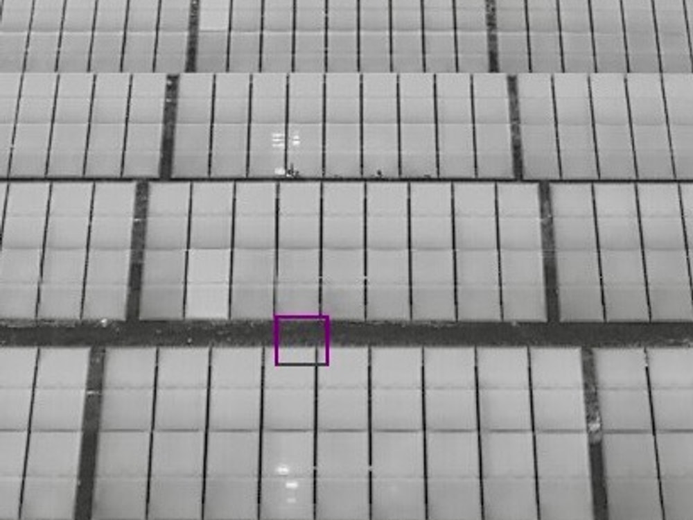 Radiometric thermal aerial frame of the same solar array rows with a flagged module highlighted, pinpointing a hot-spot anomaly