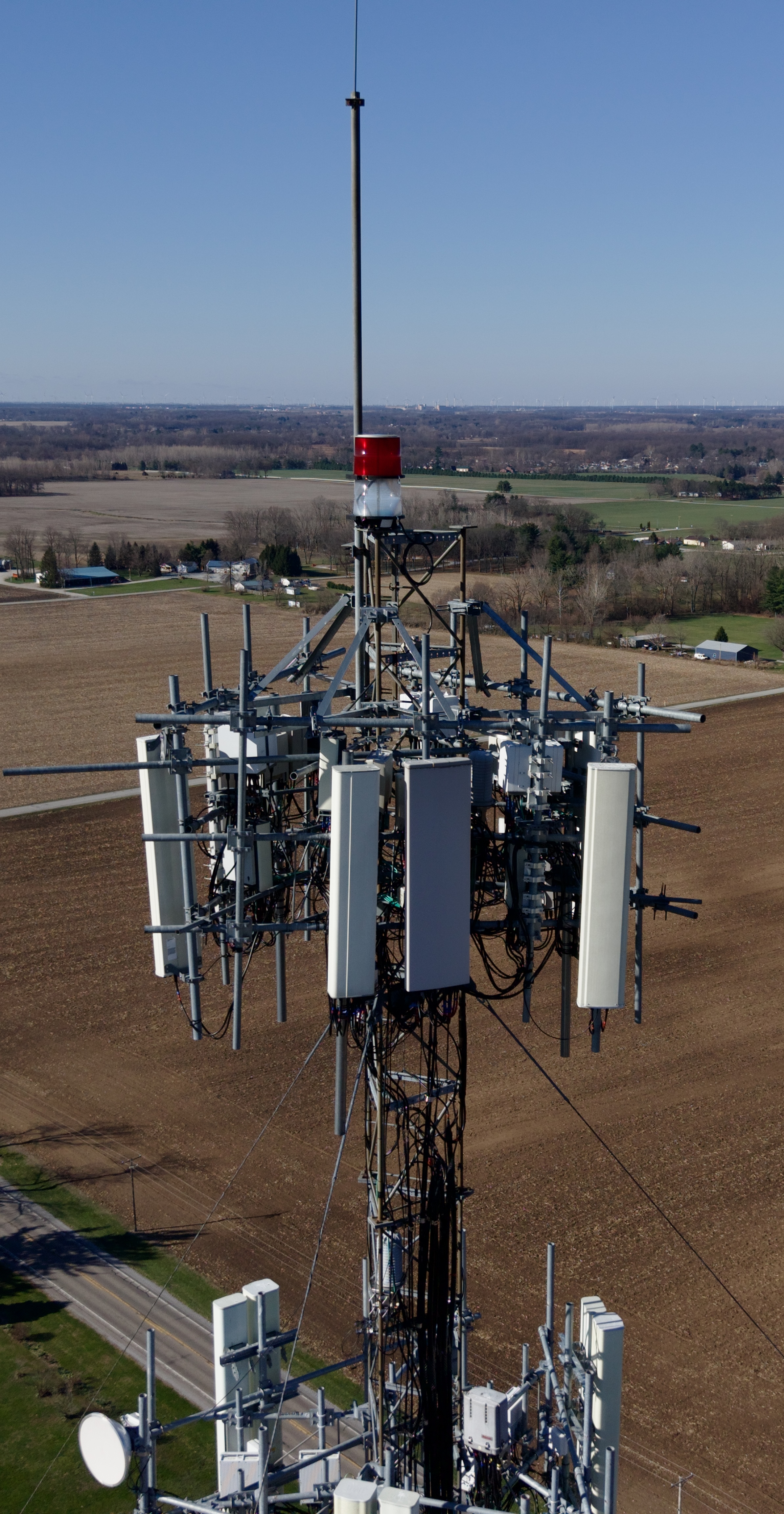 Cell tower top loaded with panel antennas and radios, captured head-on from the air