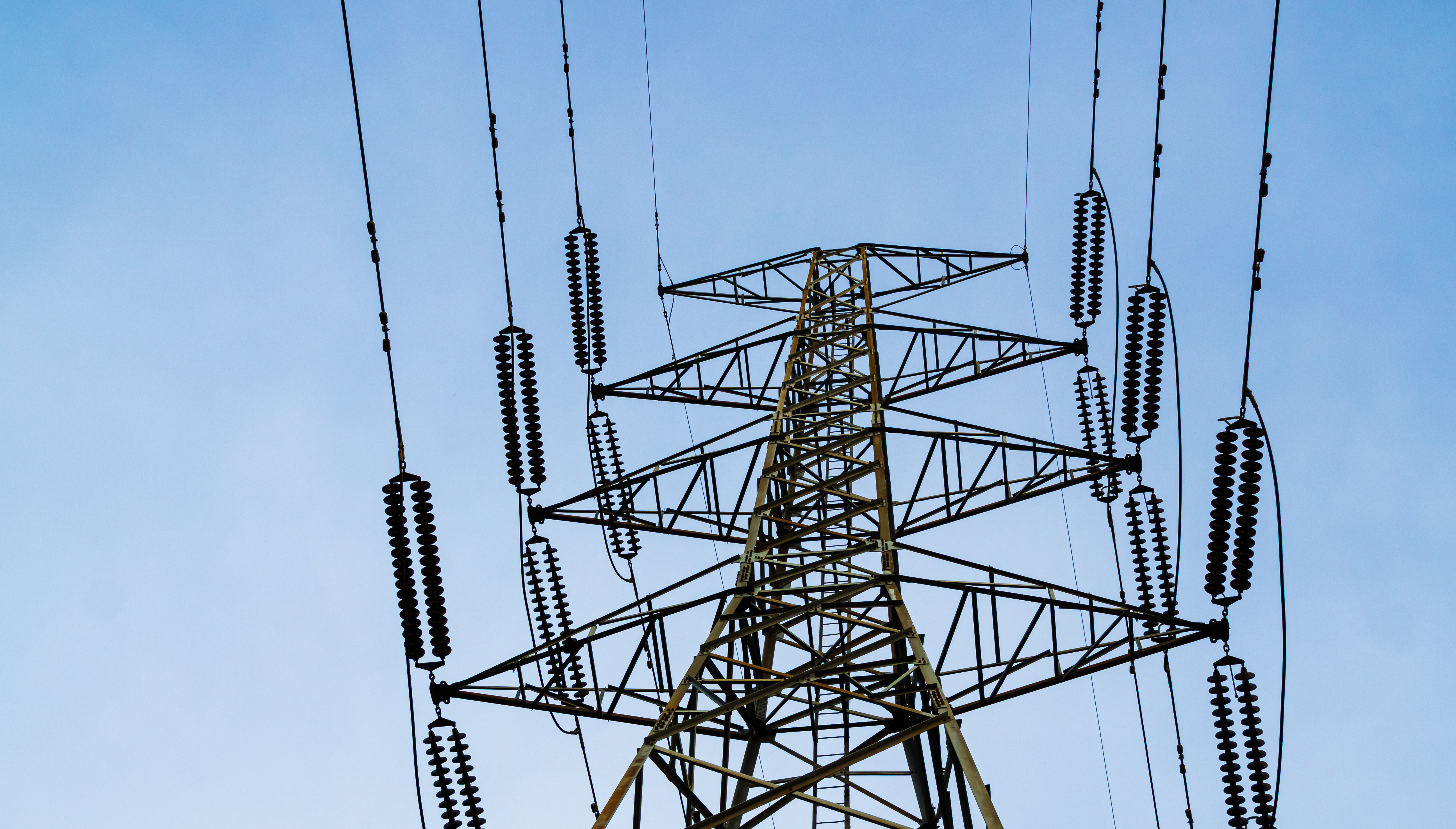 Steel lattice high-voltage transmission tower with insulator strings and conductors against a clear blue sky