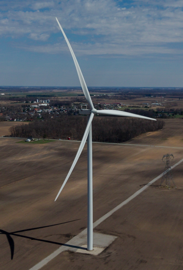 Utility-scale wind turbine tower, nacelle, and blades captured up close from the air