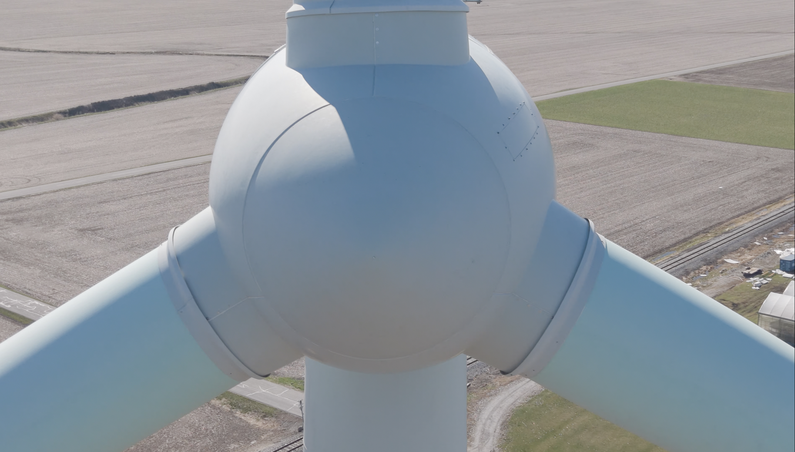 Extreme aerial close-up of a wind turbine hub, spinner, and blade roots showing surface and joint detail
